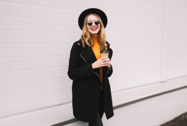 Mola zamanı! Şık kahve fincanı şehirde gri duvar arka plan üzerinde yürüme ile gülümseyen genç kadın