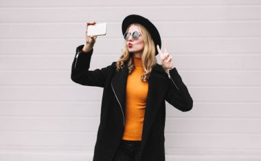 Moda, teknoloji ve insan kavramı - selfie resim smartphone, kırmızı dudaklar üfleme şık bir kadın model alarak serin kız şehir gri duvar arka plan üzerinde poz bir hava öpücük gönderir.