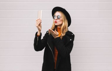 Moda, teknoloji ve insan kavramı - mutlu güzel kadın yanında smartphone, şık bir kadın model kırmızı dudaklar gönderir şehir gri duvar arka plan üzerinde poz bir hava öpücük üfleme selfie fotoğraf çekimi