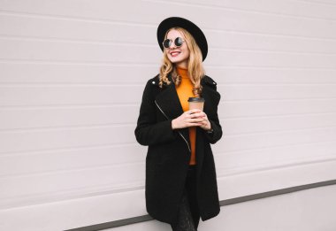 Mola zamanı! Kahve Kupası uzağa gri duvar arka plan üzerinde şehirde görünümlü şık gülümseyen genç kadın