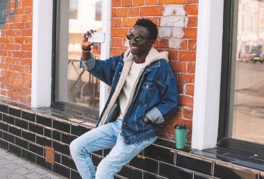 Mutlu gülümseyen Afrika adam selfie fotoğraf yanında kahve fincanı City ile oturan smartphone sokak çekimi