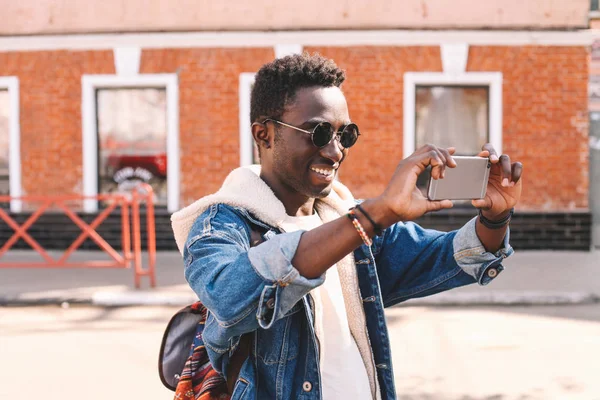 愉快的微笑的非洲男子在城市街道上通过智能手机拍摄自拍照片 — 图库照片
