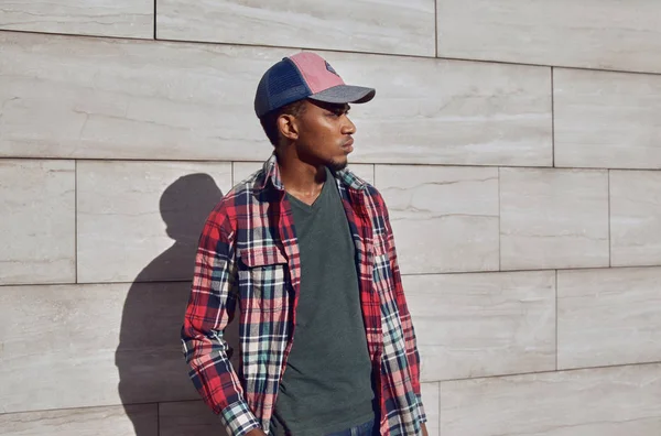 Homem africano elegante vestindo camisa xadrez vermelho, boné de beisebol, looki — Fotografia de Stock