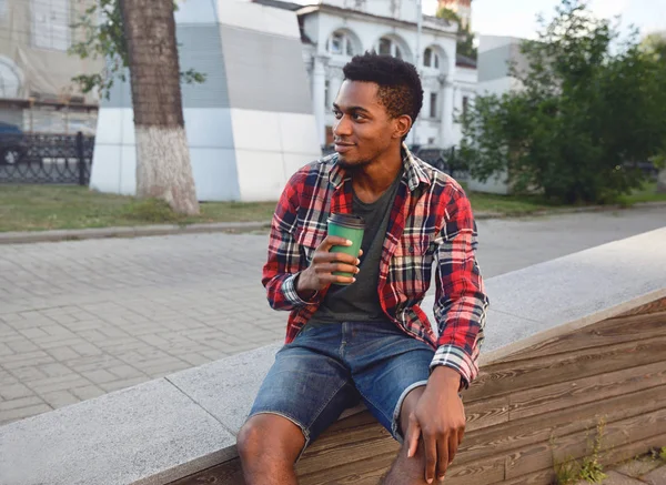 Hora da pausa! Jovem homem africano com xícara de café sentado na cidade st — Fotografia de Stock