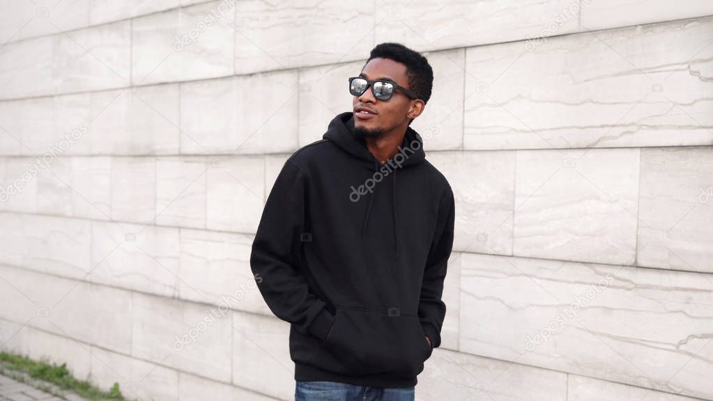 Portrait african man in black hoodie, sunglasses walking on city