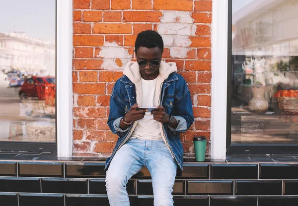 Hombre africano urbano fresco con teléfono inteligente, taza de café sentado en ci —  Fotos de Stock