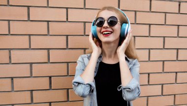 Kablosuz kulaklıklı mutlu bir kadının portresi. Müzik dinliyor. Siyah yuvarlak bir şapka giyiyor.