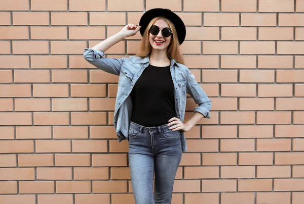 幸せな笑顔若い女性身に着けている黒丸帽子 カジュアルジーンズジャケット 女性モデルポージング上のレンガの壁の背景 — ストック写真