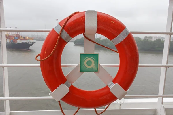Red life buoy on cruise ship with container ship on background bad weather