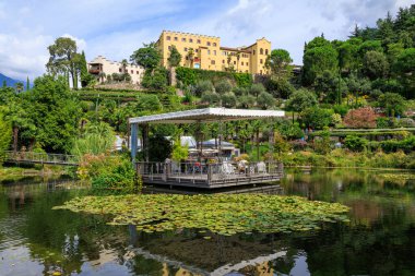 Merano, South Tyrol, İtalya yakınlarındaki Nilüfer havuzu, çiçekler, ağaçlar ve bitkilerle dolu Trauttmansdorff Kalesi panoraması 