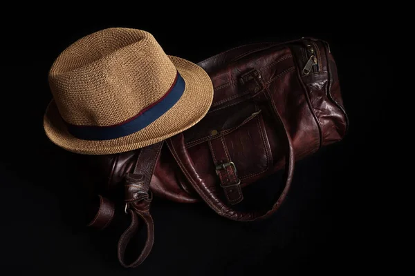 A jazz retro brown hat and a leather duffel brown bag isolated in black background