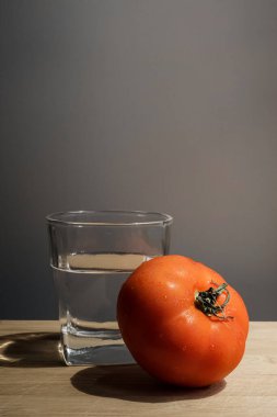 Mükemmel durumda taze domates ve ahşap bir altlığın üzerinde bir bardak su.