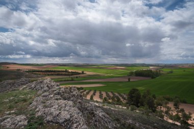 Castilla La Mancha 'nın yeşil tarlalarının manzarası Ucles, Cuenca, İspanya' daki bir tepenin tepesinden bulutlarla dolu bir gökyüzünün altında.