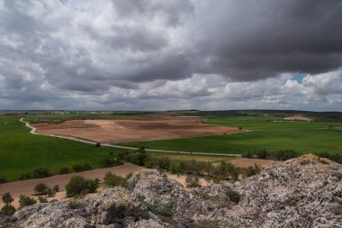 Castilla La Mancha 'nın yeşil tarlalarının manzarası Ucles, Cuenca, İspanya' daki bir tepenin tepesinden bulutlarla dolu bir gökyüzünün altında.