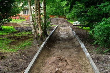 Henüz çamur ve su birikintileriyle tamamlanmamış yayaların yolu ve kenarlarında taş kaldırımlar. Sağında dört huş ağacı ve arka planda Saint-Petersburg, Rusya 'da bir apartman dairesi var.