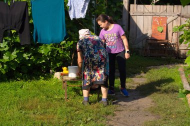 11-12 yaşlarında bir kız, büyükannesinin yanında duruyor ve arkasını dönüp bize bakarken ona yardım ediyor. Belki de bu Mordova köyünün bahçesinde çamaşır yıkıyorlardır. Rus köyünün günlük yaşamı