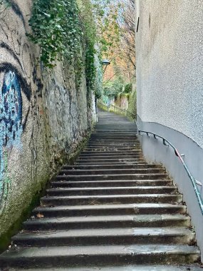 Lyon, Fransa - 23 Mart 2025: Notre-Dame de Fourviere Bazilikası 'na yükselen grafiti kaplı taş duvarlı dik yosunlu merdiven, şehir metaneti ve akşam güneşi altında yeşillik çerçeveli