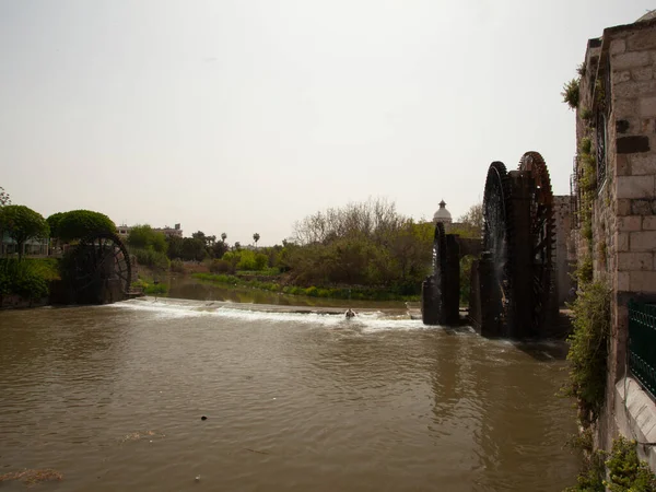 Image of the historic water wheels in Hama, Syria These are large mechanical wooden wheels called norias. They take water from orontes river and canalise it to irrigation.Panoramic Image features Norias on both sides of the river.