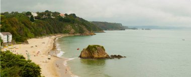Galler 'in güneybatısındaki tarihi Tenby kasabasının kuzey sahilinin panoramik manzarası. Kumsal bir uçurumun eteklerinde başlıyor ve kıyıda bir kaya parçası var..