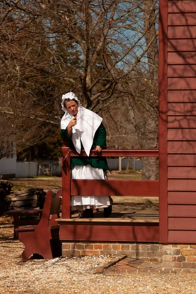 威廉斯堡 Virgina Usa 2014 一位白人殖民女性的肖像 她站在她历史性农舍的栏杆边 指着什么东西 来自威廉斯堡殖民地主题博物馆的场景 — 图库照片