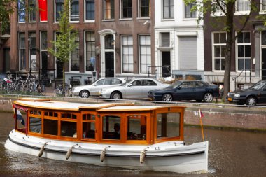 Amsterdam, Hollanda 05 / 14 / 2010: Amsterdam 'da turist taşıyan şık bir nehir teknesi. O şey. Ahşap yolcu kompartımanı var ve arkasında Hollanda bayrağı asılı. Amsterda 'da sıradan bir gün.
