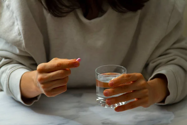 A woman is seen as she is holding a pill in one hand and a glass of water on the other hand. She is about to take the pill. A versatile image for multi purpose use in healthcare related issues.