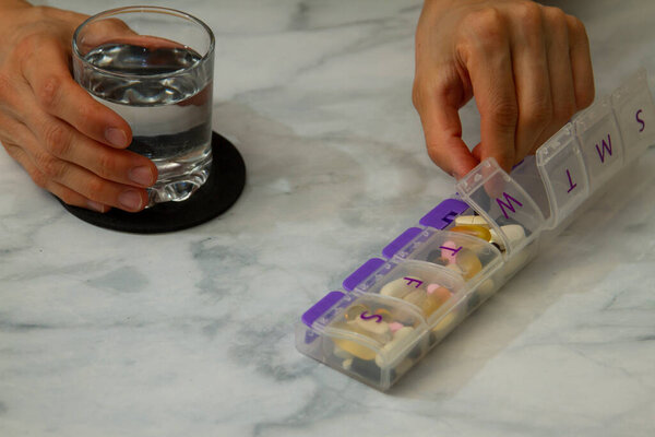 Закройте изображение женских рук, когда она протягивает руку к ящику с таблетками, где у нее есть различные лекарства на каждый день. Полезные демонстрации при хронических заболеваниях, применении нескольких препаратов или дополнений
.