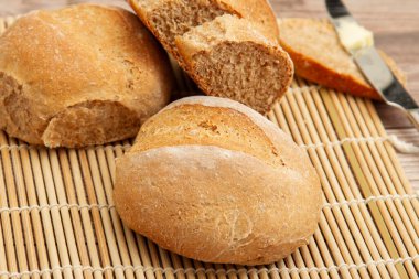 Ev yapımı tam buğday ekmeği fırından yeni çıkmış. Tahta masada bambu bir hasırın üzerinde soğuyorlar. Üzerine tereyağı sürülmüş bir tereyağı bıçağı....