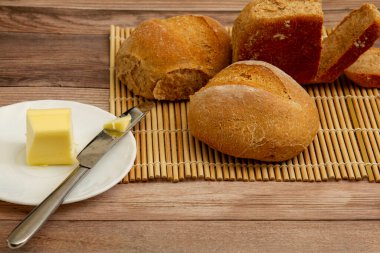 Ev yapımı tam buğday ekmeği fırından yeni çıkmış. Tahta masada bambu bir hasırın üzerinde soğuyorlar. Üzerine tereyağı sürülmüş bir tereyağı bıçağı....