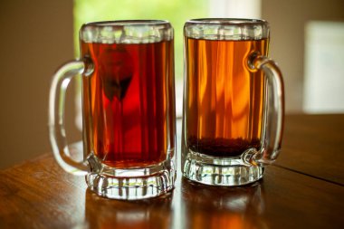 Taze siyah çayla doldurulmuş iki büyük bardak bira bardağının görüntüsünü kapat. Kupalar arka planda ağaçlarla açık bir pencere pervazında oturuyorlar..   