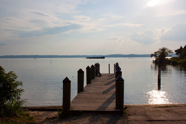 A view of the Mallows bay by Potomac River on a sunny day. Image is featuring a boat ramp and a wooden pier with docking posts. This place is home to over a hundred shipwrecks including the one seen.