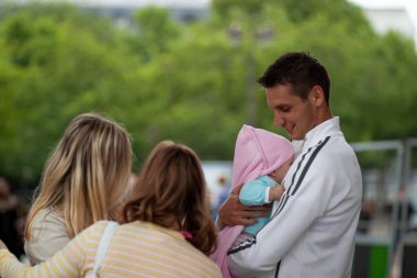Paris, Fransa 06 / 12 / 2010: Küçük tatlı kızını kucağında tutan genç ve yakışıklı bir babanın izole edilmiş bir görüntüsü. Yanında annesi ve teyzesi var. Hepsi bebeğe bakmaya çalışıyor.