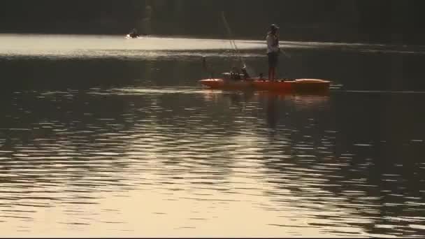メリーランド州 米国2010 2010年8月8日 帽子をかぶっている若い男がカヤックに立ち 湖で釣りをしている 背景には別の人がパドリングしている — ストック動画