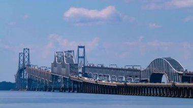 Chesapeake Bay Köprüsü 'ndeki yoğun trafiği gösteren bir gündüz telefonu zaman atlamalı görüntüsü. Belgede köprünün sütunları ve süspansiyonları ve altından geçen teknelerin ayrıntılı görüntüsü yer alıyor..