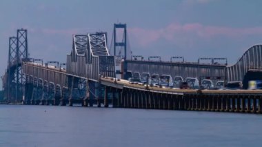 Chesapeake Bay Köprüsü 'ndeki yoğun trafiği gösteren bir gündüz telefonu zaman atlamalı görüntüsü. Belgede köprünün sütunları ve süspansiyonları ve altından geçen teknelerin ayrıntılı görüntüsü yer alıyor..