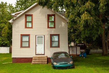 Chesapeake City, MD, USA 08 / 25 / 2020: Büyük bir bahçesi olan tek bir aile evinin önüne sisli farları olan eski, paslı bir araba bırakıldı. Burası bir sürü ağacın olduğu bir kırsal bölge. 
