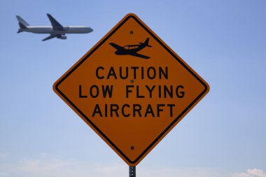 Stensville, MD 08 / 18 / 2020: Uçak logosuna sahip 'Dikkat Düşük Uçan Uçak' yazan yerel bir havaalanı yakınındaki yol tabelası. Bulanık yolcu uçağının tabelanın arkasından uzak bir mesafeden geçtiği görülüyor..