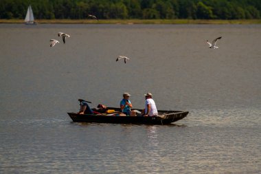 Eastern Neck Adası, 08 / 30 / 2020: Üç kişi küçük ahşap bir balıkçı teknesinde dinleniyor. Biri uyuyor, diğer ikisi konuşuyor. Bir su kuşu sürüsü üzerlerinden uçup yiyecek çalmaya çalışıyor..