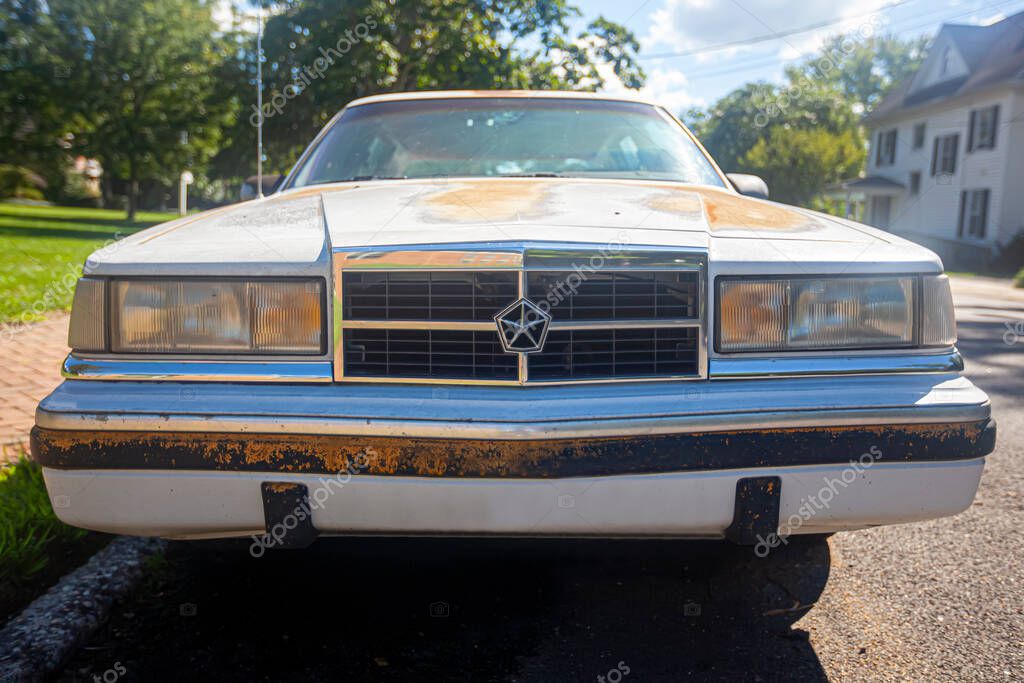 Chestertown, MD, USA 08/30/2020: Front view of a very old white rusty Dodge Dynasty LE car parked outside on the street. It has rusted and chipped paint and corrosion on the front panel.