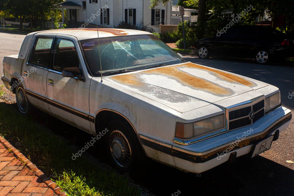 Chestertown, MD, USA 08/30/2020: Side view of a very old white rusty Dodge Dynasty LE car parked outside on the street. It has rusted and chipped paint and corrosion all over it