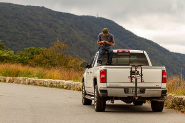 Shenandoah Vadisi, VA, ABD, 09 / 27 / 2020: Bir adam, sürücü kabininde oturan beyaz bir GMC Sierra kamyonetinin bagajında telefonuyla oynuyor. Araç manzaralı bir yere park edilmiş..