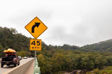 Potomac Nehri üzerindeki Sandy Hook köprüsünde sarı bir sağ viraj. İşaret levhası, yaklaşan viraj için saatte 45 mil hız limitini öneriyor. Appalachian dağları arka planda görülür.
