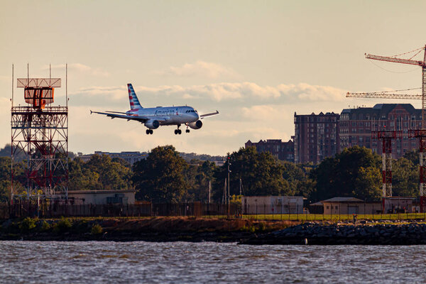 Washington DC, USA 10 / 03 / 2020: An Airbus A321 airplane by American Airlines is landing descending to land on Ronald Reagan National Airport. Он проходит мимо радарной башни на закате..