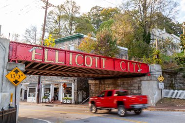Ellicott City, MD, ABD 10 / 07 / 2020: Şehrin girişindeki B & O demiryolu köprüsünün yanında büyük harflerle yazılmış Ellicott City tabelasına hoş geldiniz. Buradan geçen eski evler ve arabalar görülüyor..