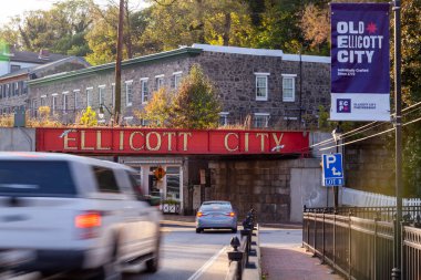 Ellicott City, MD, ABD 10 / 07 / 2020: Şehrin girişindeki B & O demiryolu köprüsünün yanında büyük harflerle yazılmış Ellicott City tabelasına hoş geldiniz. Buradan geçen eski evler ve arabalar görülüyor..