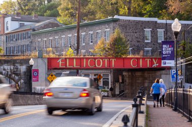 Ellicott City, MD, ABD 10 / 07 / 2020: Şehrin girişindeki B & O demiryolu köprüsünün yanında büyük harflerle yazılmış Ellicott City tabelasına hoş geldiniz. Buradan geçen eski evler ve arabalar görülüyor..