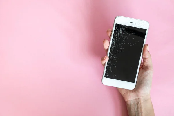 Smartphone with broken screen in hand on pink background
