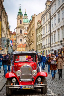 Prag, Çek Cumhuriyeti - 06.01.2019: Red retro car and Church of Saint Nicolas veya kostel svateho Mikulase, Prag, Çek Cumhuriyeti'nde insanlarla mostecka caddesinden görünümü