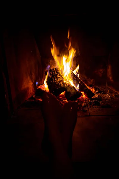 Bare legs of young woman are heated by open fire in fireplace — Stock Photo, Image