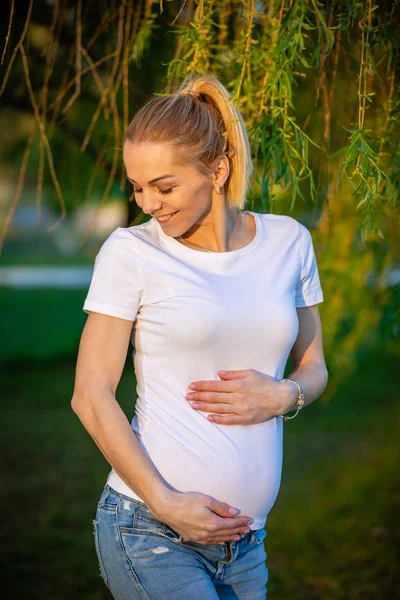 Porträtt av en lycklig och stolt gravid ung kvinna som tittar på hennes mage i parken vid Sunrise, New Life Concept — Stockfoto